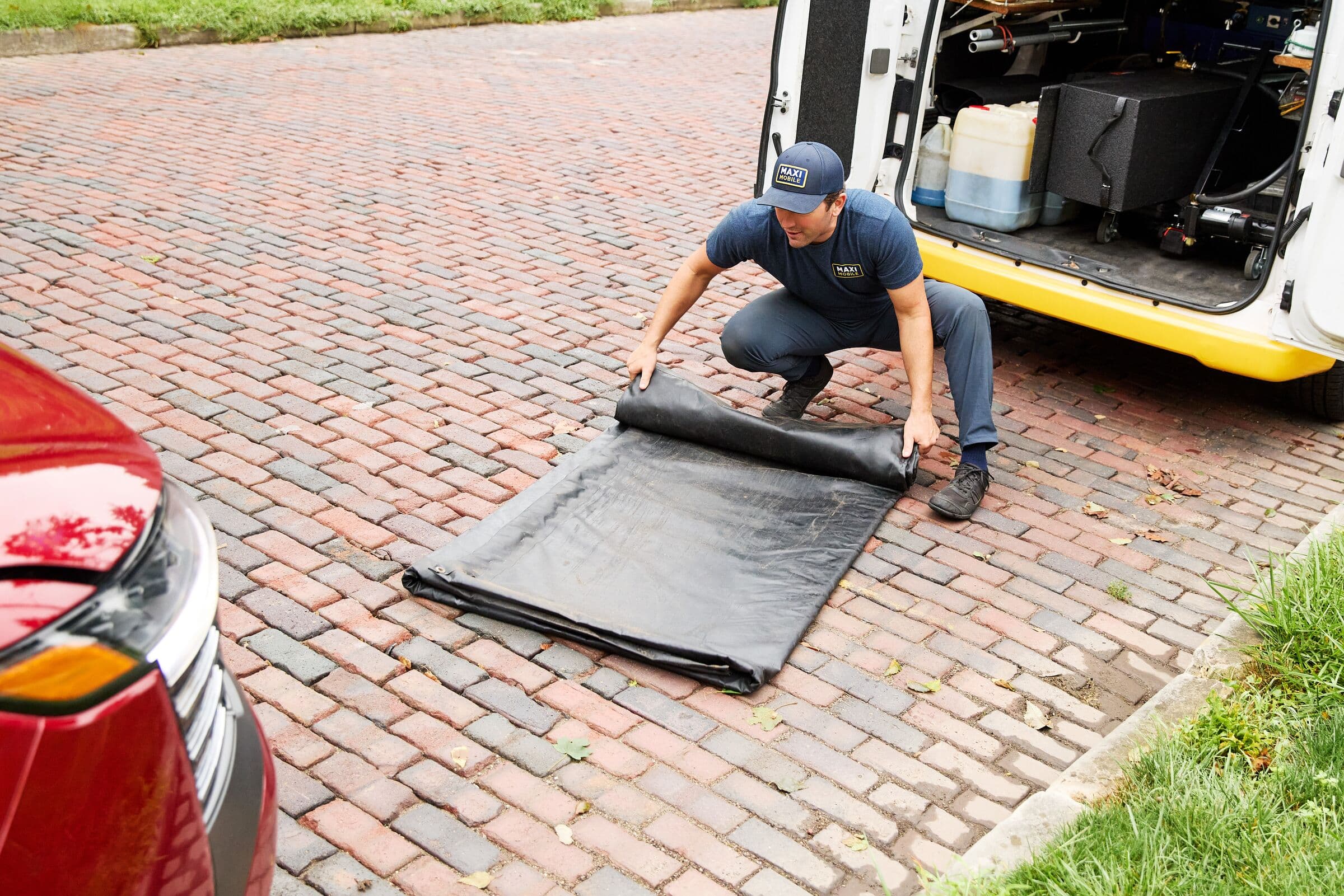 A MAXI technician rolling out a drip mat on a brick driveway before service