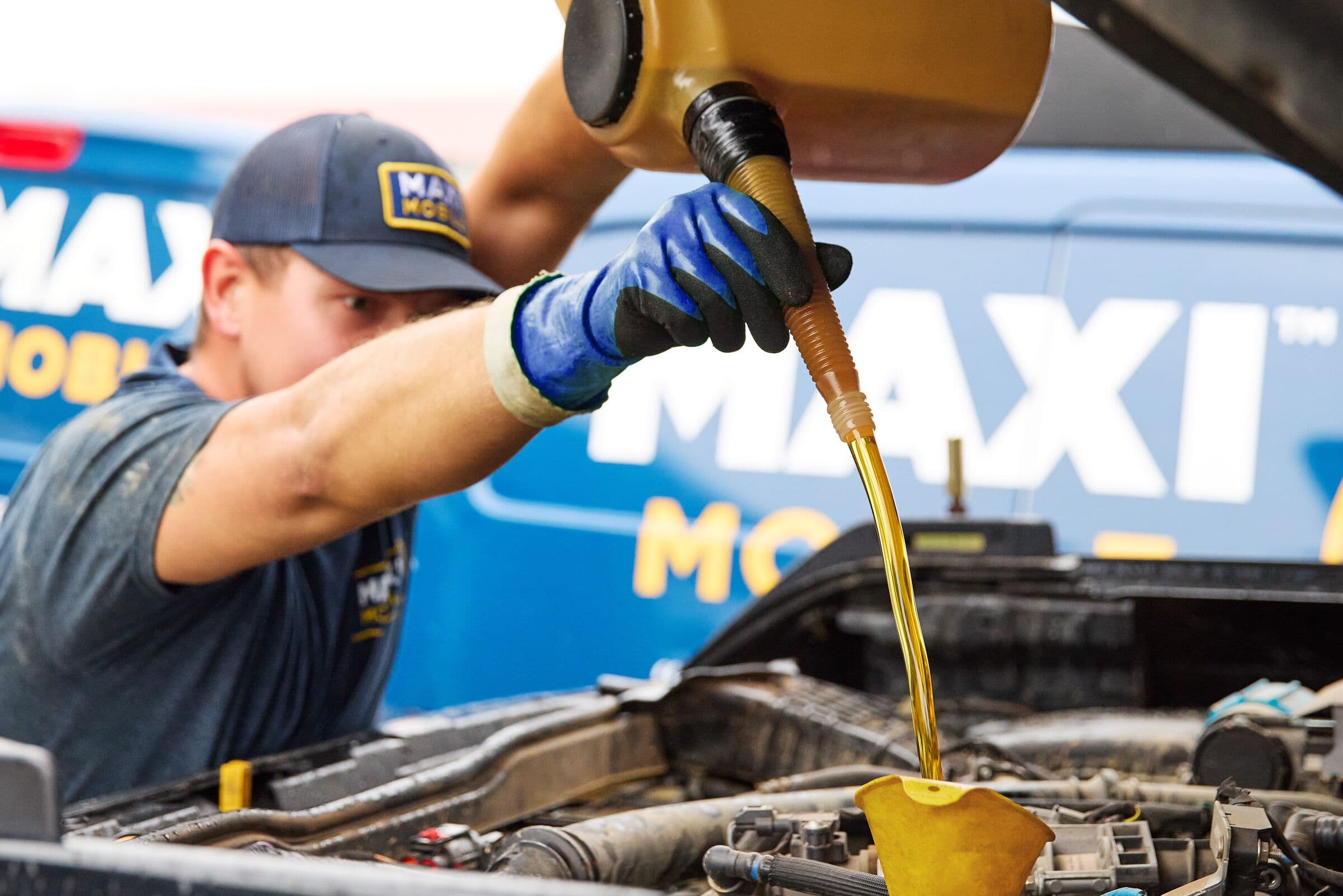 A MAXI technician pouring full-synthetic oil in front of a MAXI service van