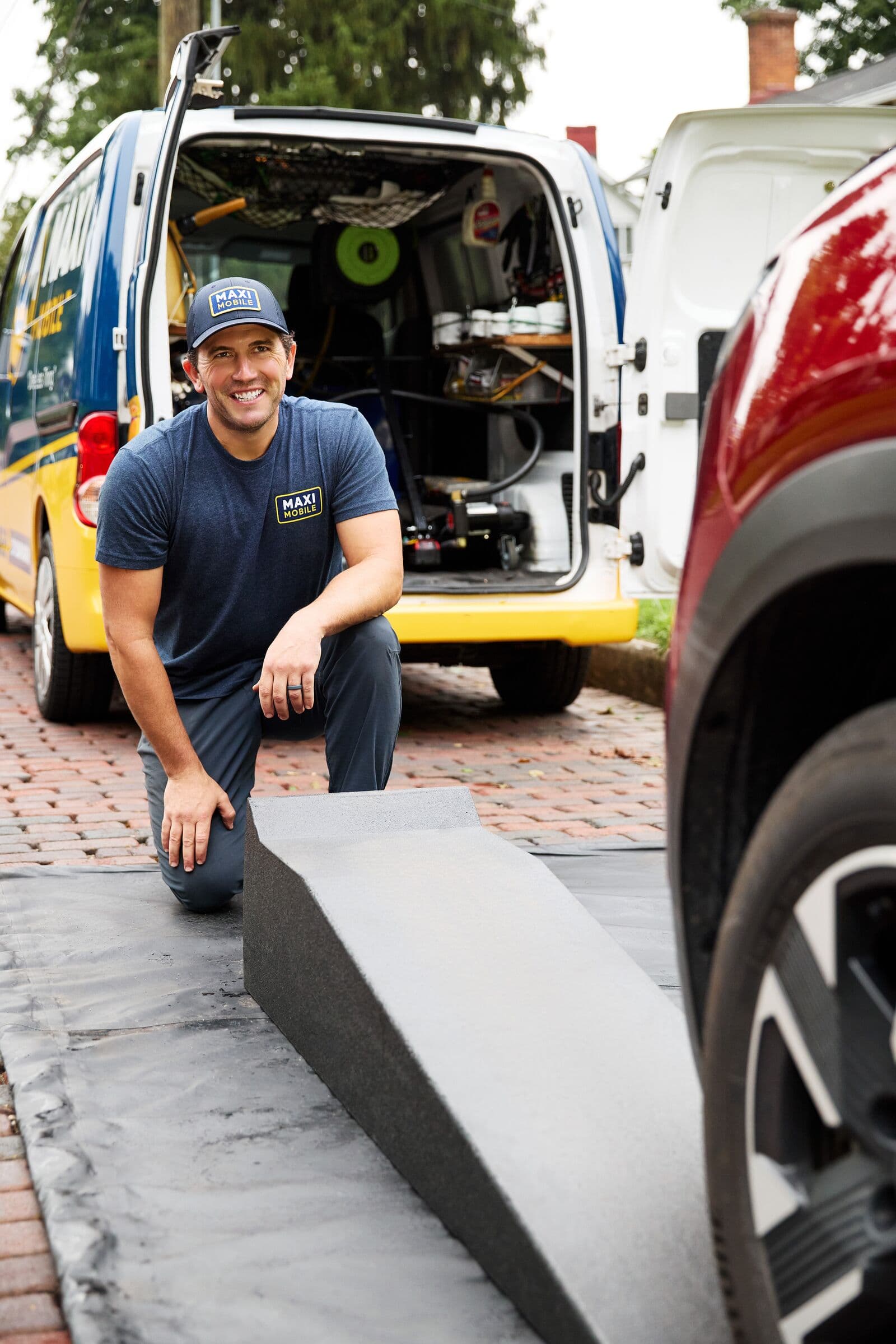 A MAXI technician setting out ramps and a drip mat beside the service van